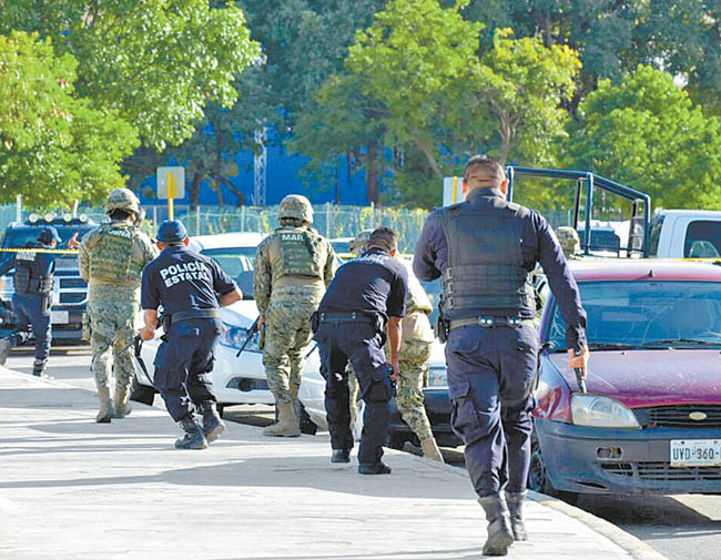 Marinos y policías estatales se resguardan para repeler el ataque de los sicarios. 