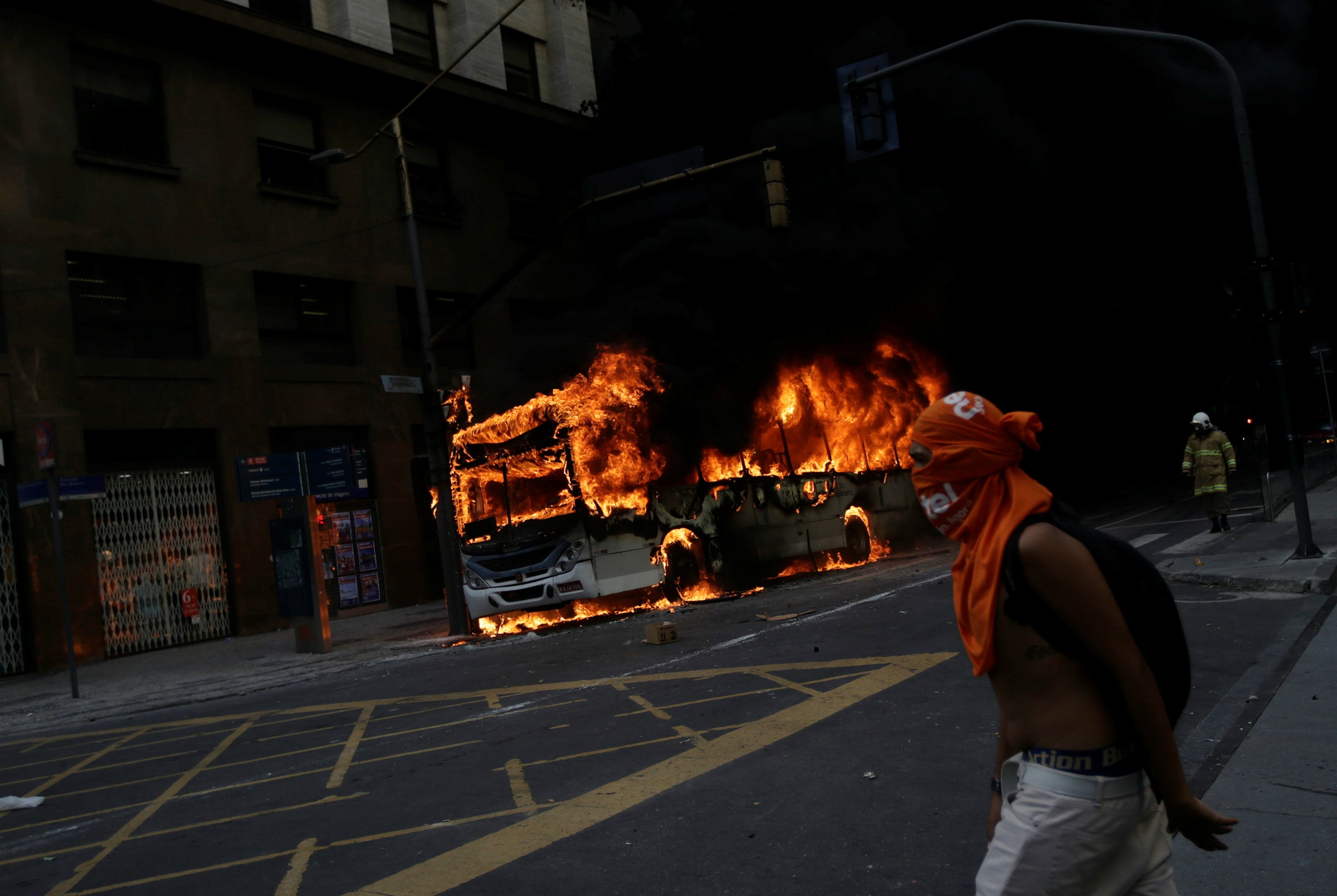 Un manifestante anti-gobierno pasa por un autobús que arde después de un enfrentamiento con policías antidisturbios, durante una protesta contra el go