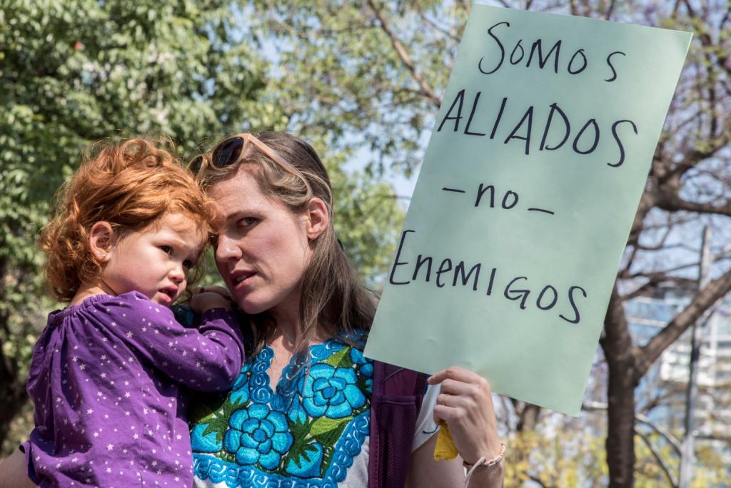 Una estadunidense con su hija en brazos sostiene una pancarta frente a la embajada de EU en México contra la retórica de Donald Trump.