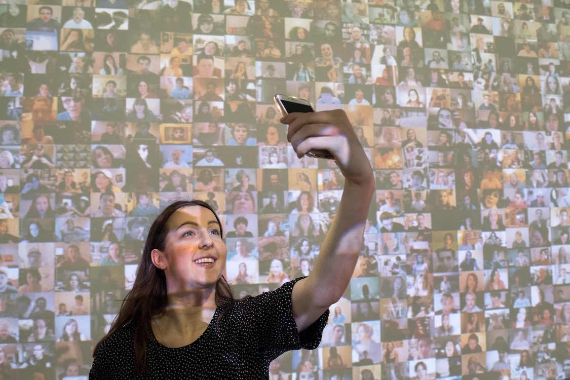 Una asistente posa junto a la video instalación "Hello World!", del artista Christopher Baker.