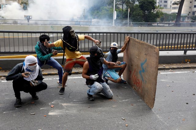 Manifestantes se resguardan y responden con piedras durante un enfrentamiento con la Policía Nacional Bolivariana.
