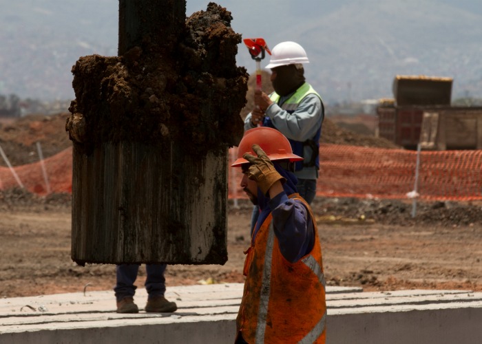 El martillo hidráulico que ayuda a la colocación de pilotes en el suelo como base de construcción es vigilado por trabajadores y topógrafos en el luga