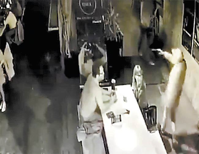 Uno de los asaltantes amaga con pistola a dos personas en una mesa. 
