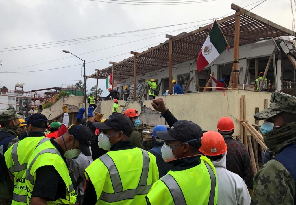 Rescatistas levantan el puño para pedir silencio cuando escuchan a alguien atrapado.