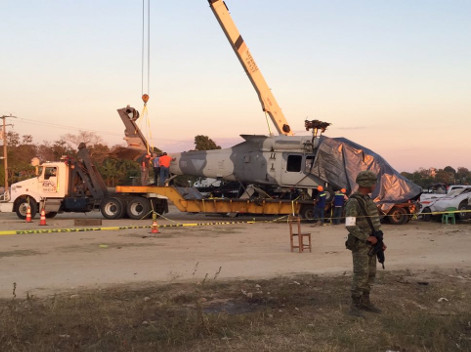 Militares retiran con una grúa la estructura del helicóptero y la cubren con una manta de lona gris y la suben a un camión de redilas.