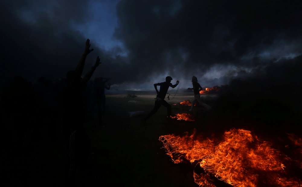 Los palestinos se ven entre el humo de las llantas quemadas en la frontera con Israel, durante los choques con las fuerzas hebreas en la Franja de Gaz