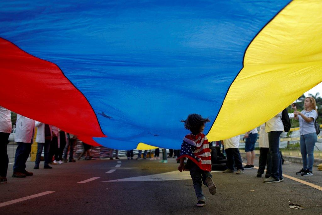 Venezuela - Un niño con una bandera de Estados Unidos pasa debajo de una venezolana durante una manifestación. REUTERS / Marco Bello