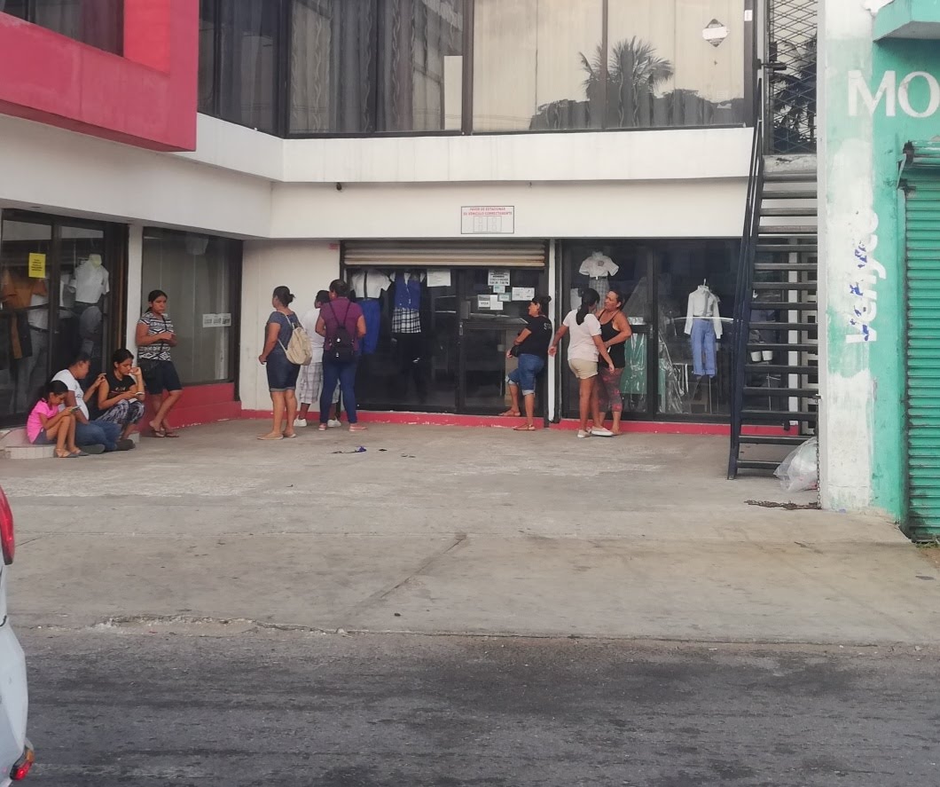 Padres de familia hacen fila afuera de una tienda de uniformes escolares.