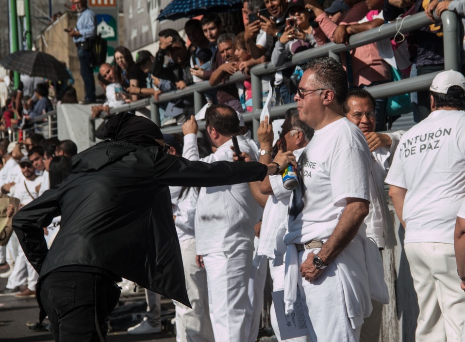 Un encapuchado pinta la playera de un integrante del 'Cinturón de Paz' durante la marcha del 2 de octubre. (Cuartoscuro)