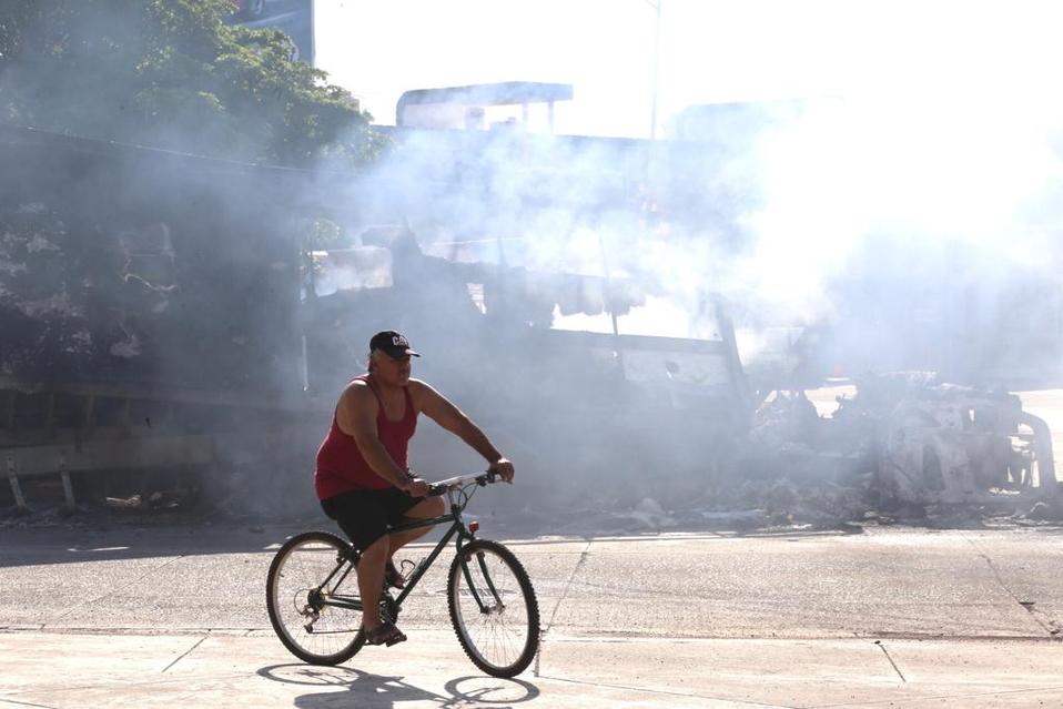 Un hombre recorre Culiacán en bicicleta frente a los vehículos quemados. (Jorge Craballo)