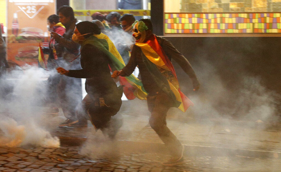 Manifestantes corren en medio de gases lacrimógenos disparados por la policía durante una protesta. (AP)