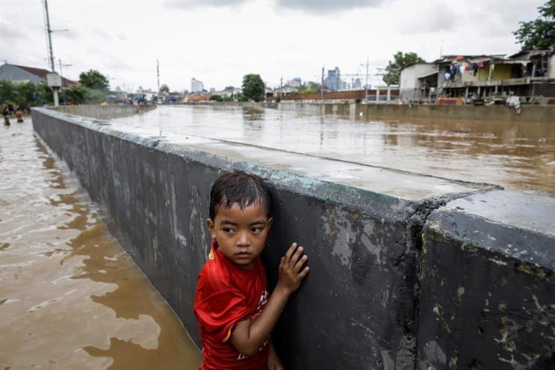 Un niño se protege tras un muro en una carretera inundada de Yakarta. (AFP)