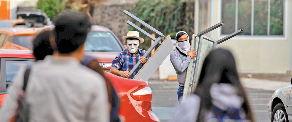 Un joven enmascarado y otro embozado cargan mesas para armar una barricada dentro de la Preparatoria 2. (Gerardo Luna/Notimex)