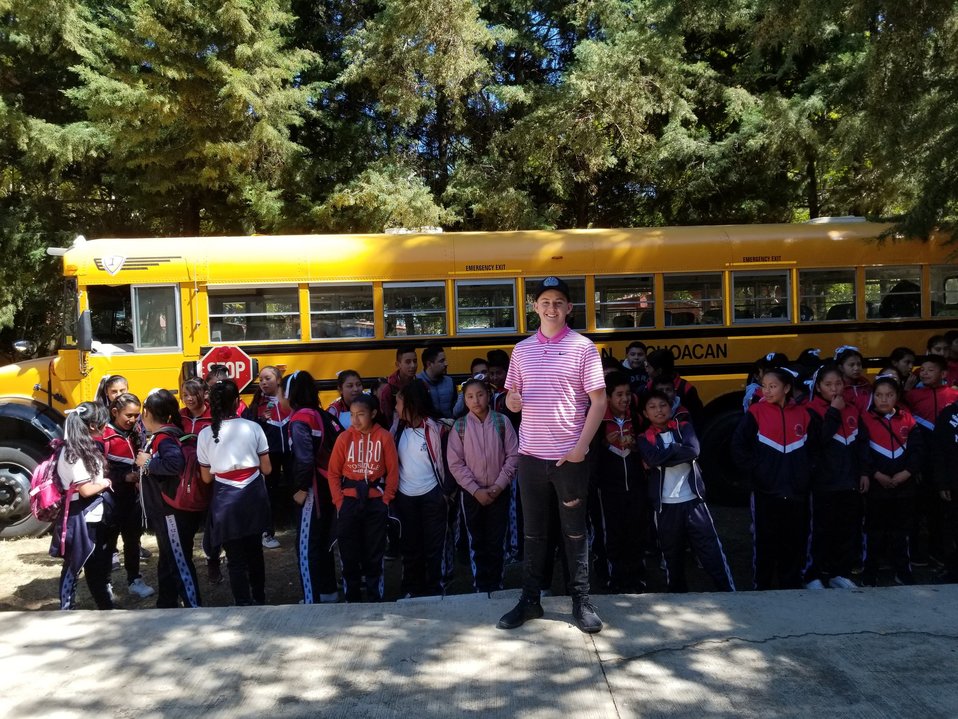 Dylan posando con el autobús y los alumnos beneficiarios (Twitter).