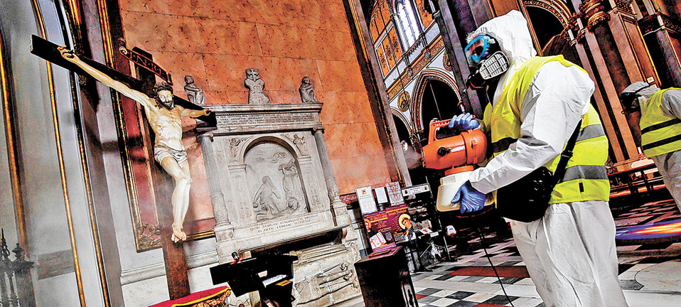 Un empleado sanitario realiza la fumigación a la imagen de un Cristo crucificado en una iglesia de Italia. (EFE)