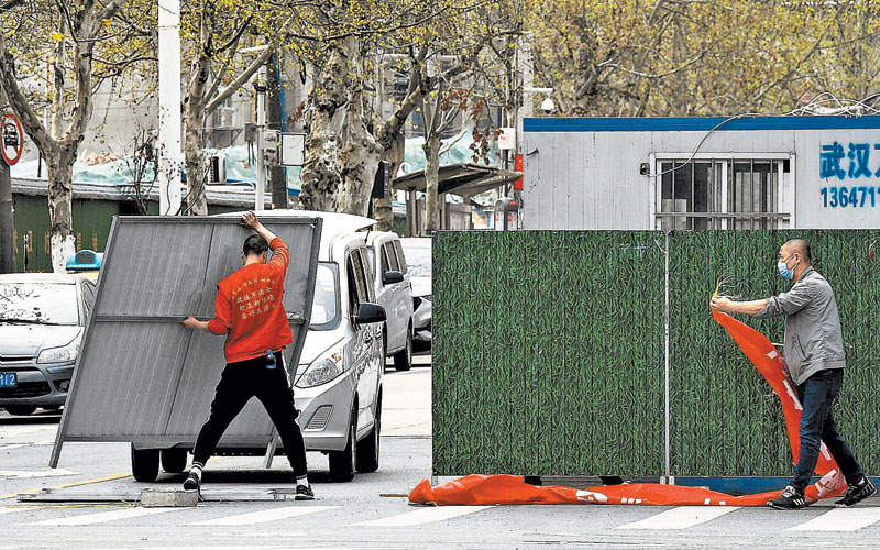 Trabajadores con mascarillas retiran las barreras en Wuhan, epicentro del brote. (REUTERS)