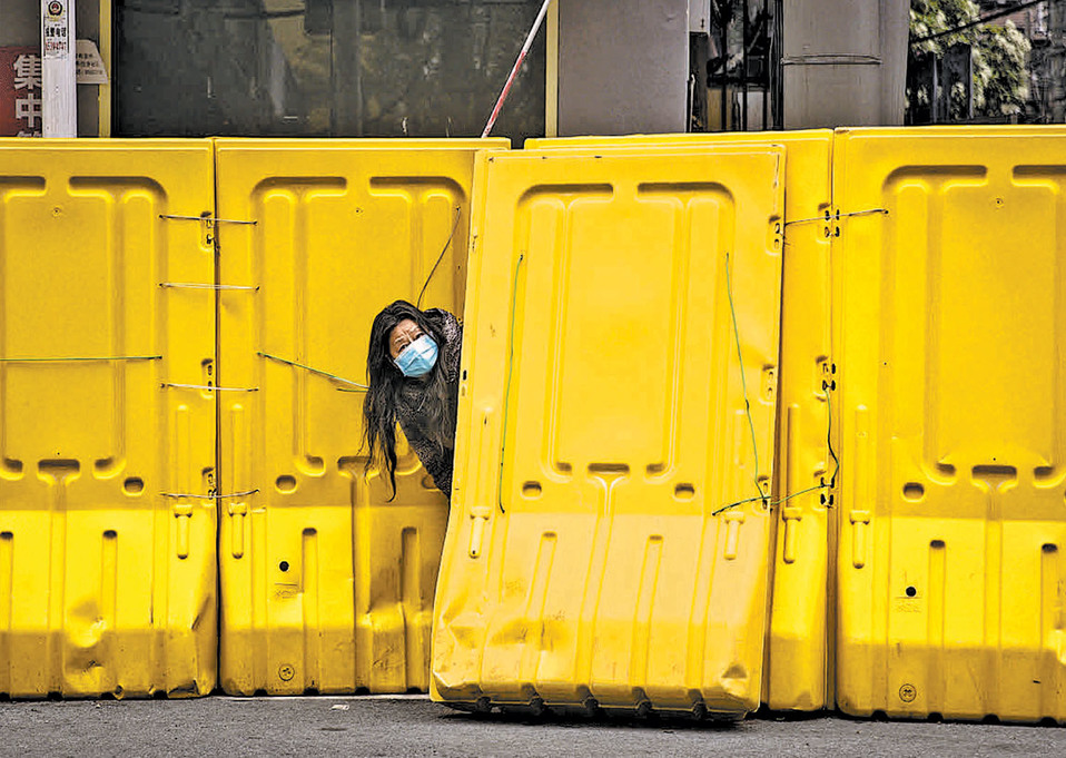 Una mujer con mascarilla asoma por una barricada para controlar el acceso a una urbanización de Wuhan. (Getty)
