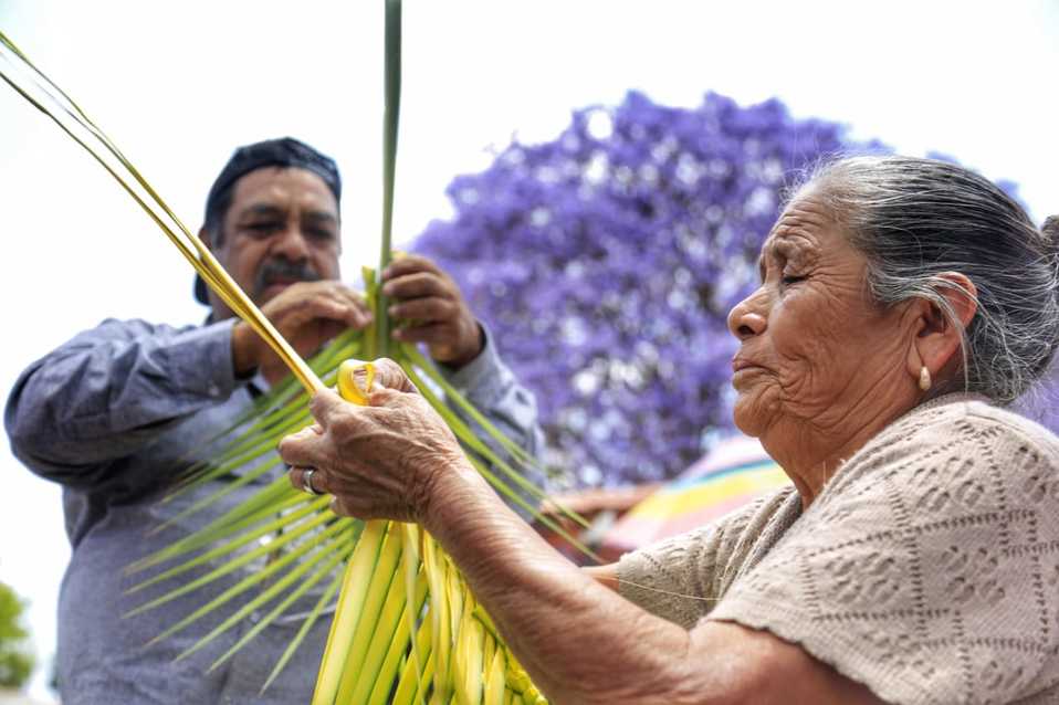 Una pareja de artesanos de Tepexi elabora artesanías de palma en el zócalo para los fieles. (Andrés Lobato)