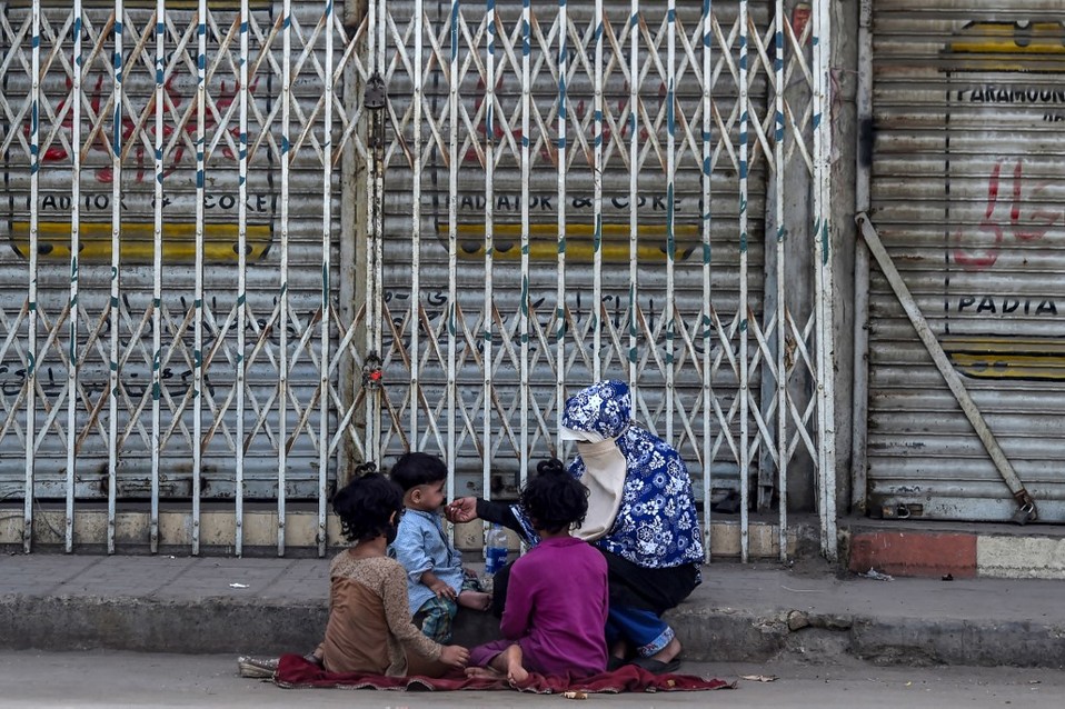 En Pakistán, una mujer le da de comer a sus hijos en las solitarias calles tras la cuarentena que vive el país. (AFP)