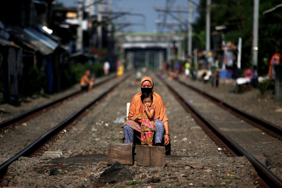 Indonesia. Una mujer con una máscara fácil y su hijo se sientan frente a las vías del tren durante la imposición de restricciones por covid-19. (Reute
