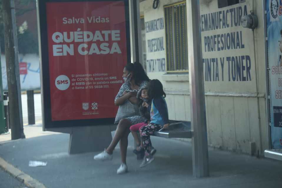 Mujer y dos niños con cubrebocas esperan en una parada de autobús. (Juan Carlos Bautista)