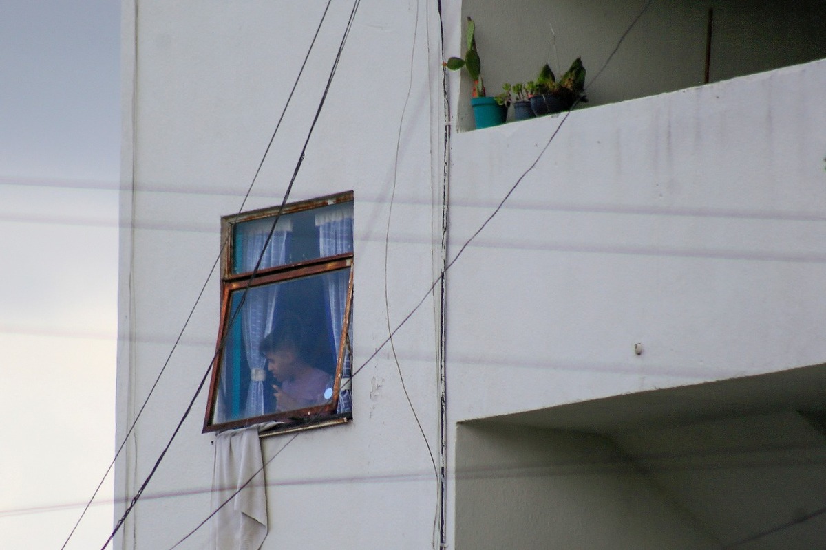 Un joven estudiante se asoma desde la ventana de un departamento en una unidad habitacional. (Andrés Lobato)