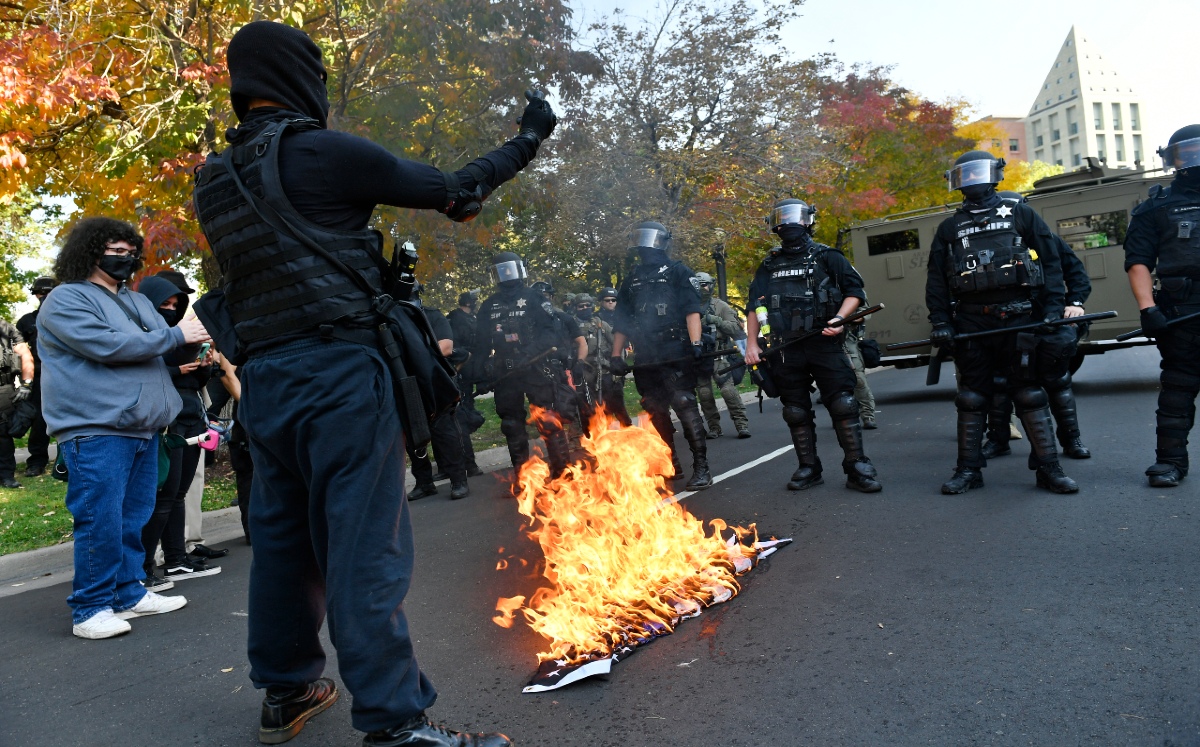 Manifestantes queman una bandera de la policía frente a agentes. / AP