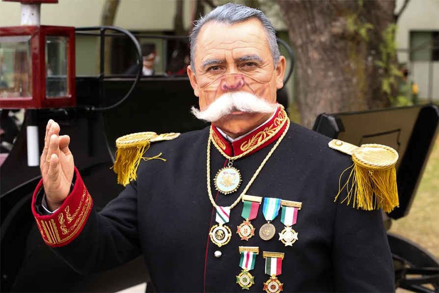 Un abundante bigote de material sintético luce el  cubrebocas de quien representa a Porfirio Díaz. |Octavio Hoyos
