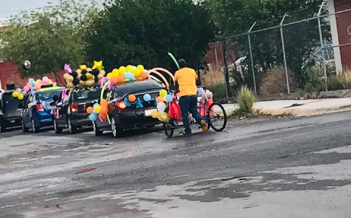 Se observa al hombre detrás de una fila de autos empujando su triciclo adornado con globos. (Especial)