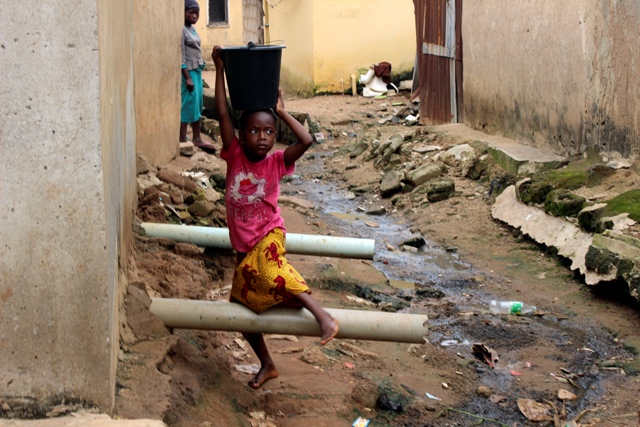 Una niña con agua sobre su cabeza pasa junto a aguas residuales entre las casas en Abuya, Nigeria. (AP)