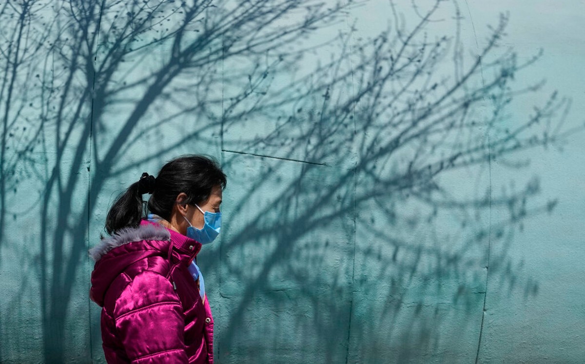 Una mujer con cubrebocas pasa junto a las sombras de un árbol en un parque en Beijing. | AP