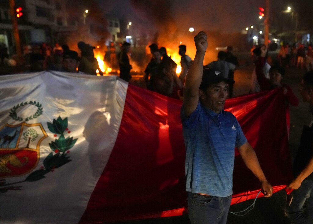 Un manifestante lanza proclamas contra el gobierno mientras otros llevan una bandera nacional durante el bloqueo de una autopista. (AP)