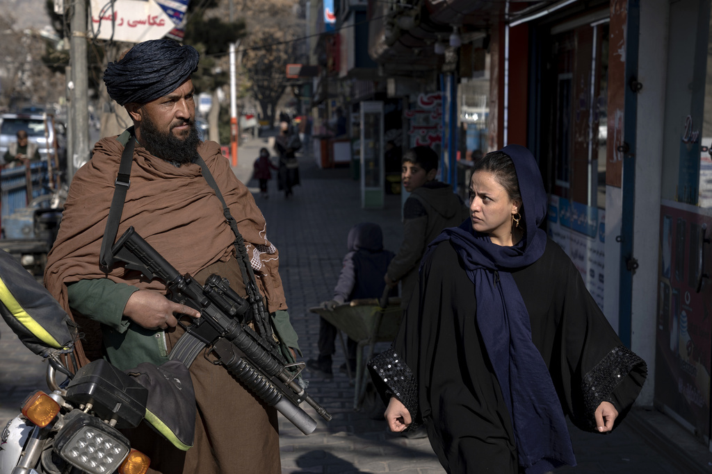Un combatiente talibán monta guardia mientras una mujer pasa caminando en Kabul, Afganistán | AP