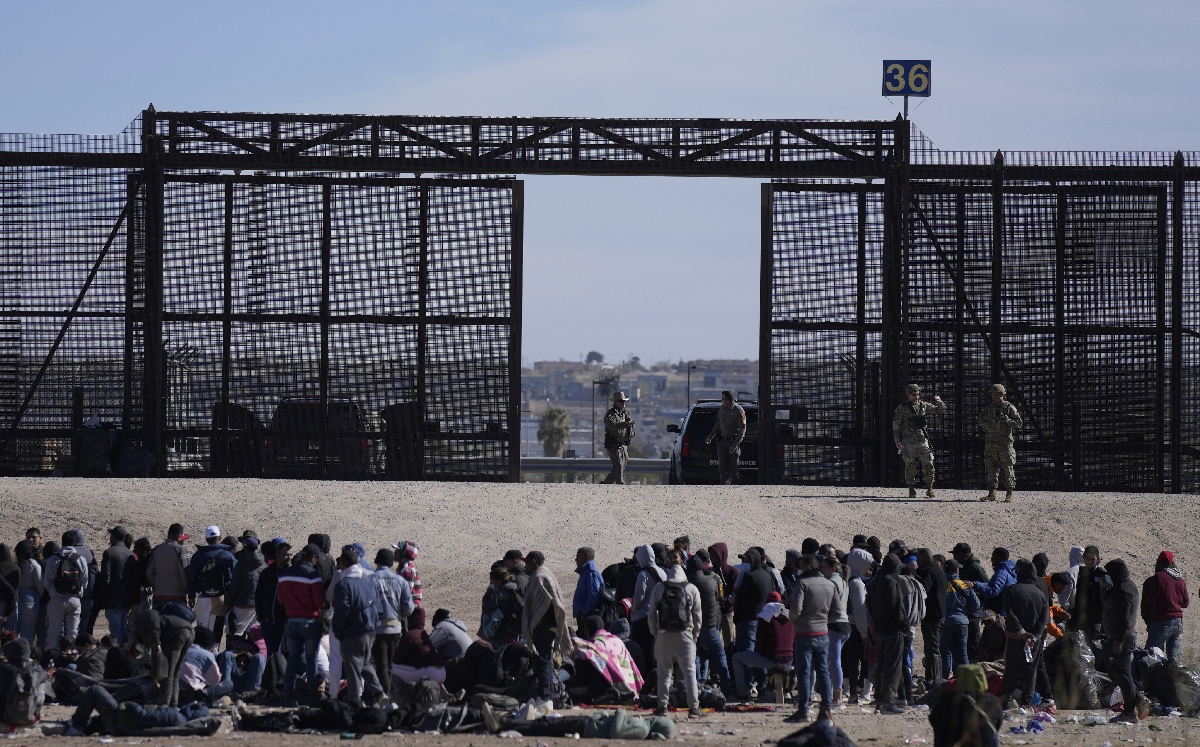 Migrantes que cruzaron la frontera desde México hacia Estados Unidos esperan a un costado del muro. | AP