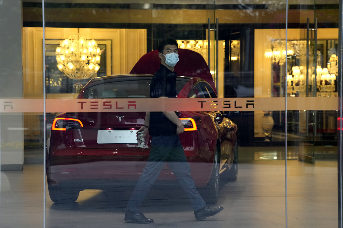 Un trabajador camina por un concesionario de Tesla en Beijing | AP