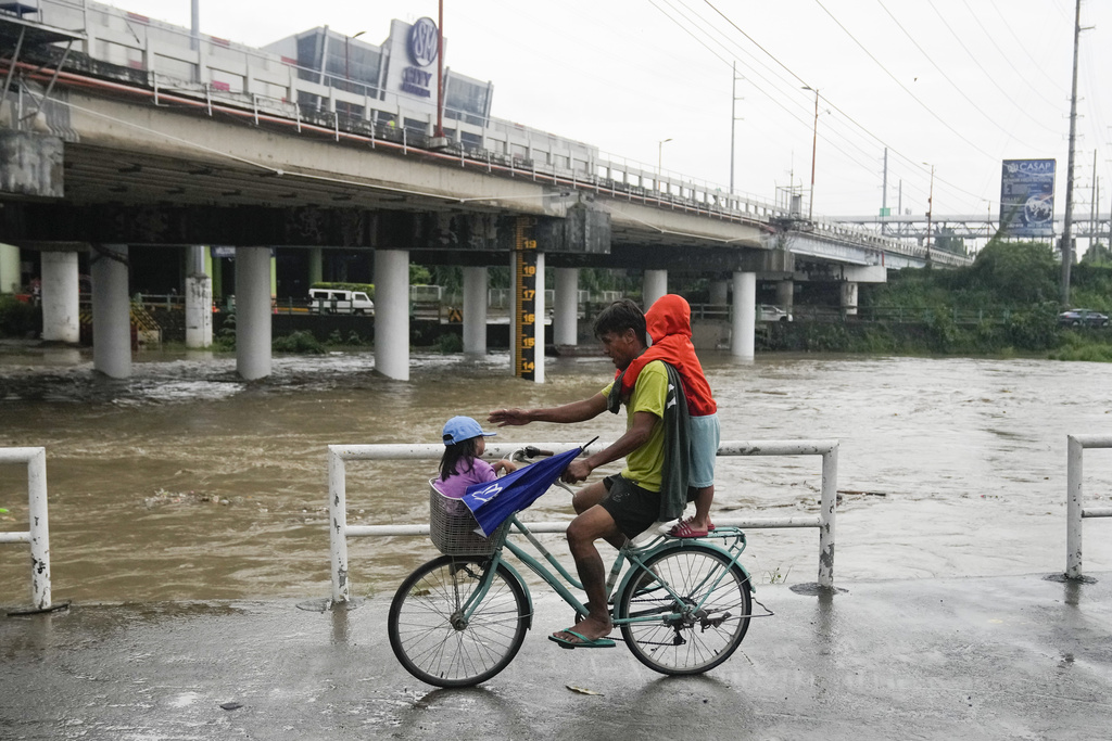 Un hombre y dos niños montan en bicicleta junto a un río crecido por las lluvias del tifón Doksuri | AP
