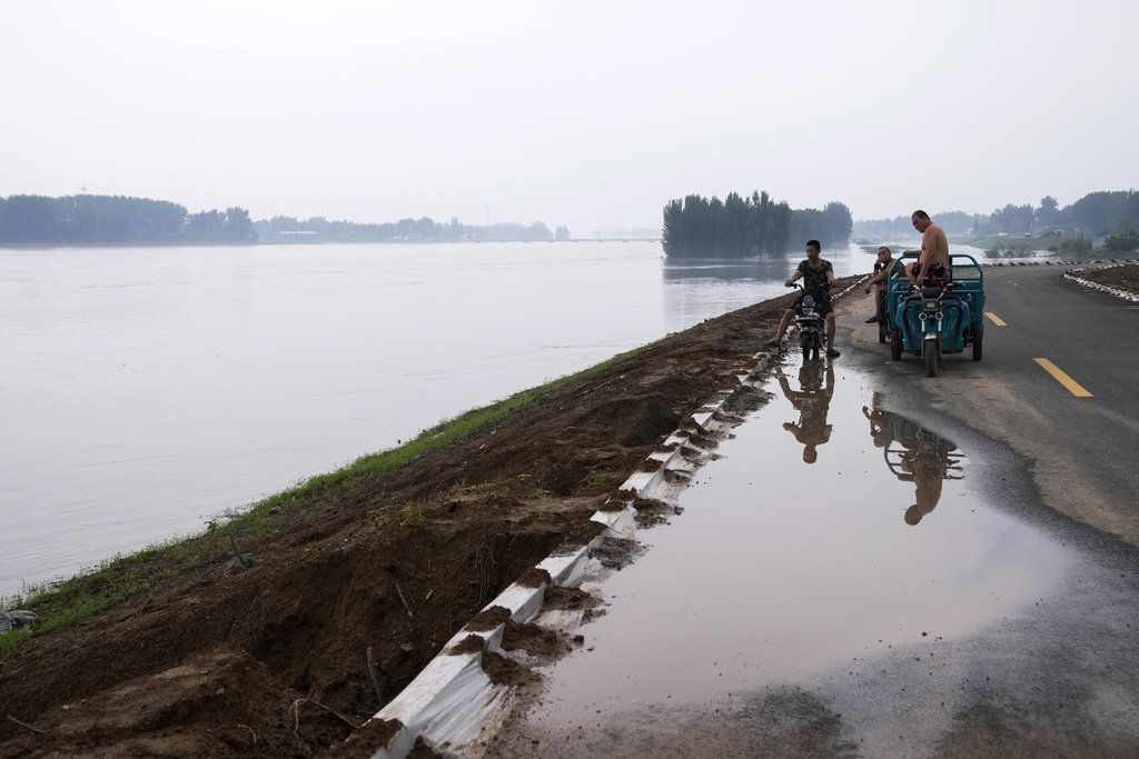 Gente mirando un río crecido que ha inundado los terrenos de cultivo en un pueblo en Langfang | AP