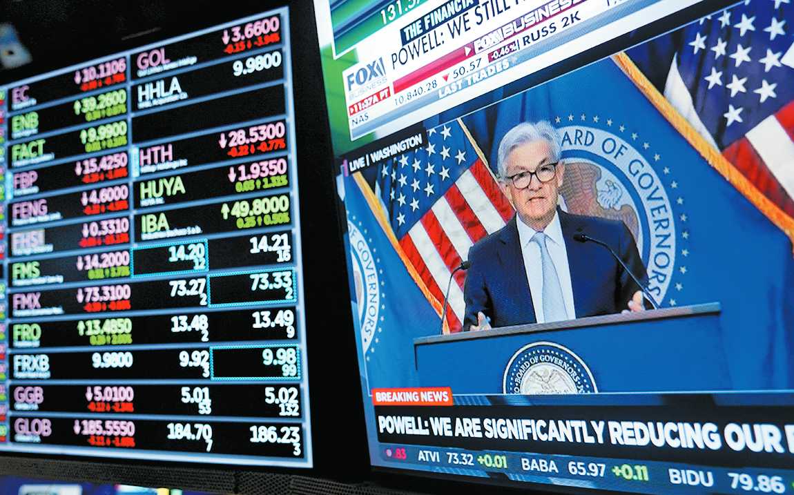 Monitores mostrando indicadores económicos; a la derecha, Jerome Powell. AP