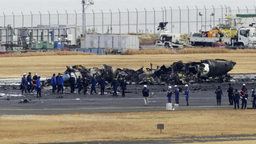Policías y bomberos se reúnen alrededor de los restos calcinados de un avión de la guardia costera japonesa en el aeropuerto de Haneda | AP
