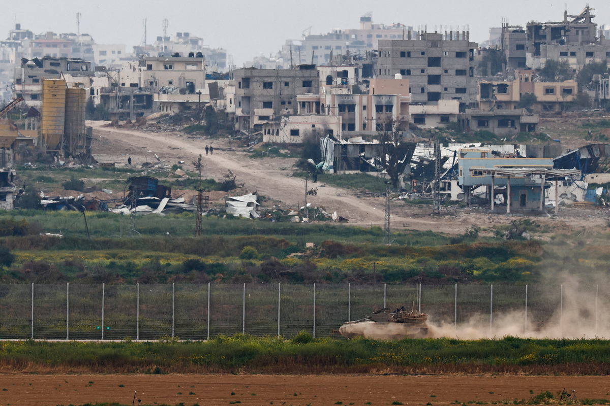 Un tanque maniobra cerca de la frontera entre Israel y Gaza en el lado israelí mientras la gente camina dentro de Gaza. | Reuters