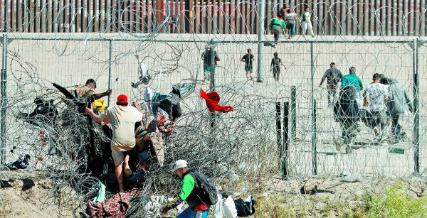 Personas intentan cruzar una alambrada de púas en la frontera que divide a México de Estados Unidos. EFE