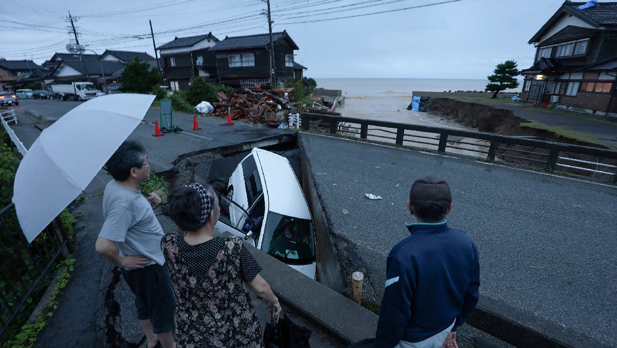 Residentes observan un automóvil atrapado en una carretera hundida después de que las fuertes lluvias en Suzu. | AFP