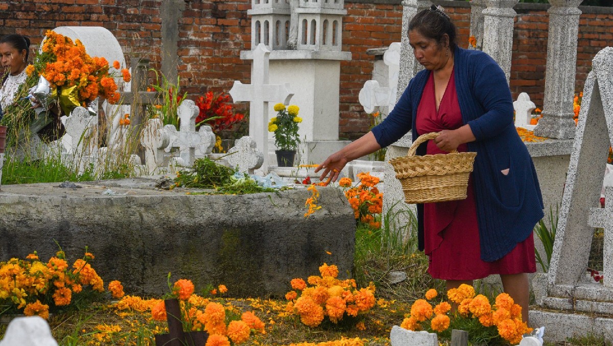 Mujer adorna con flores de cempasúchil la tumba de un familiar. | Cuartoscuro