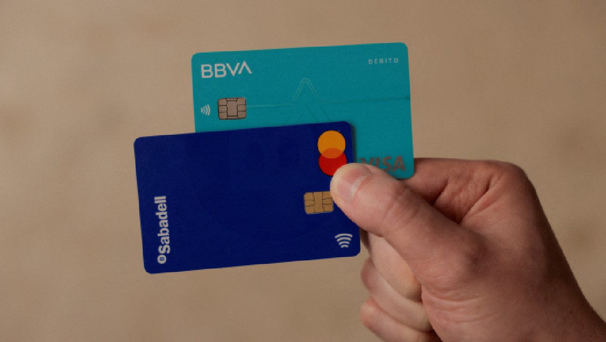 Hombre muestra sus tarjetas de débito de bancos BBVA y Sabadell, en Ronda, España. Mayo de 2024. Foto: Reuters