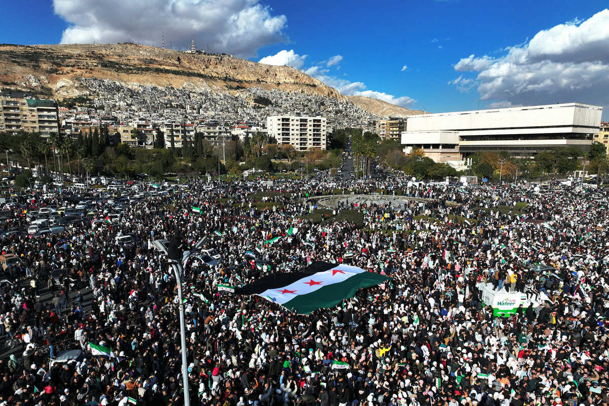 El monte Qasyoun al fondo, mientras la gente levanta una bandera siria gigante de la era de la independencia. | AFP