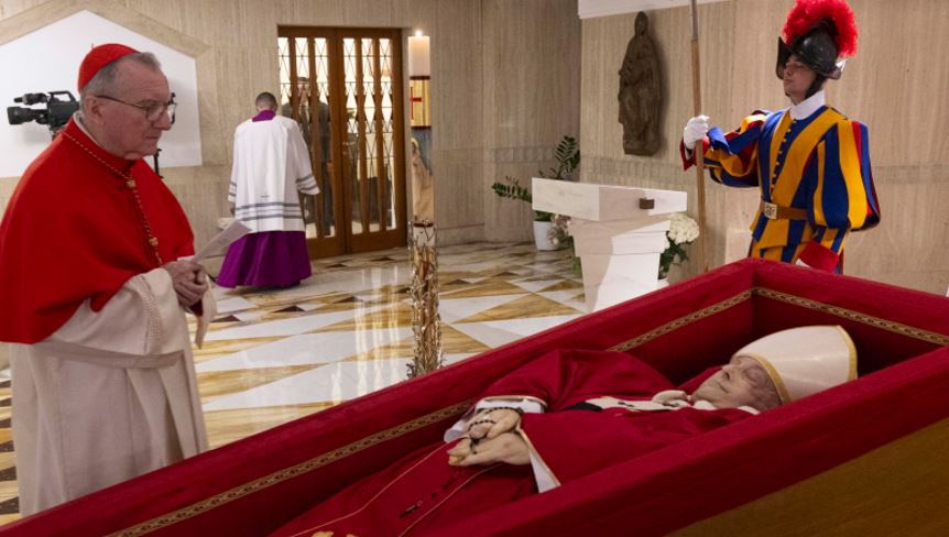 Su cuerpo yace dentro de su féretro, ataviado con una casulla roja y mitra blanca. AP