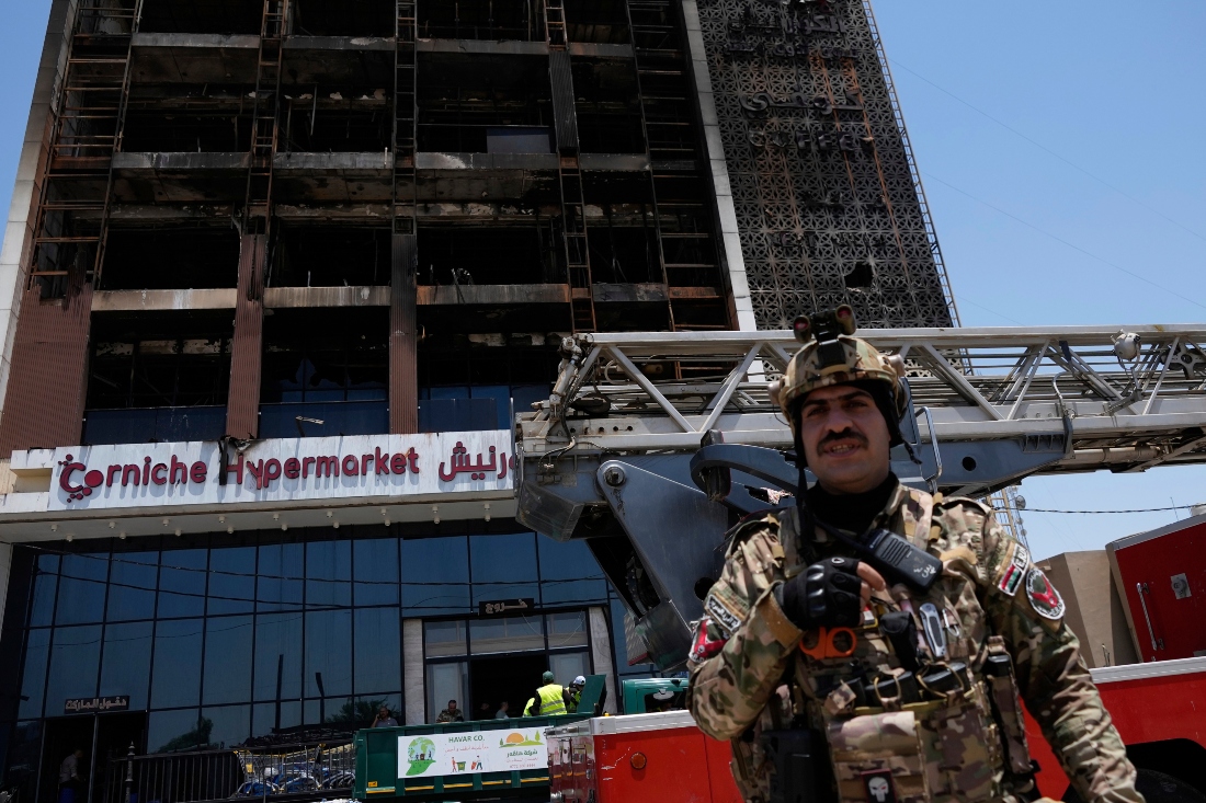 Un guarda de seguridad iraquí hace guardia delante del edificio de un hipermercado incendiado, en Kut, Irak. |AP