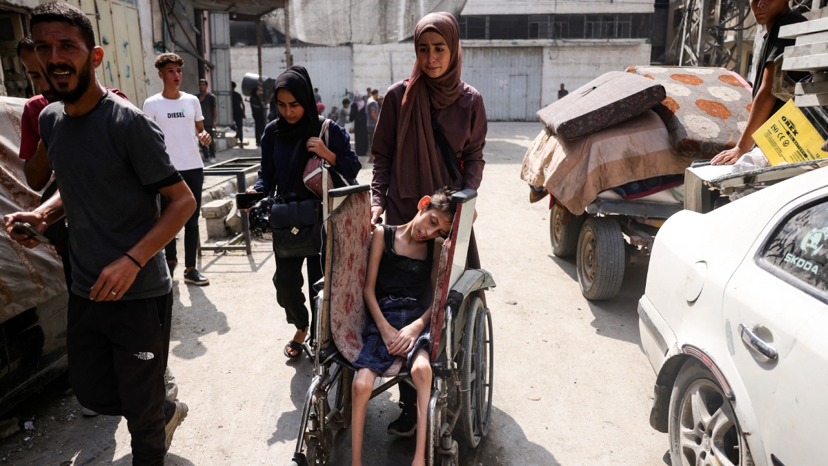 Mujer palestina empuja la silla de ruedas de un niño mientras huye con otros del barrio de Abu Iskandar. | AFP