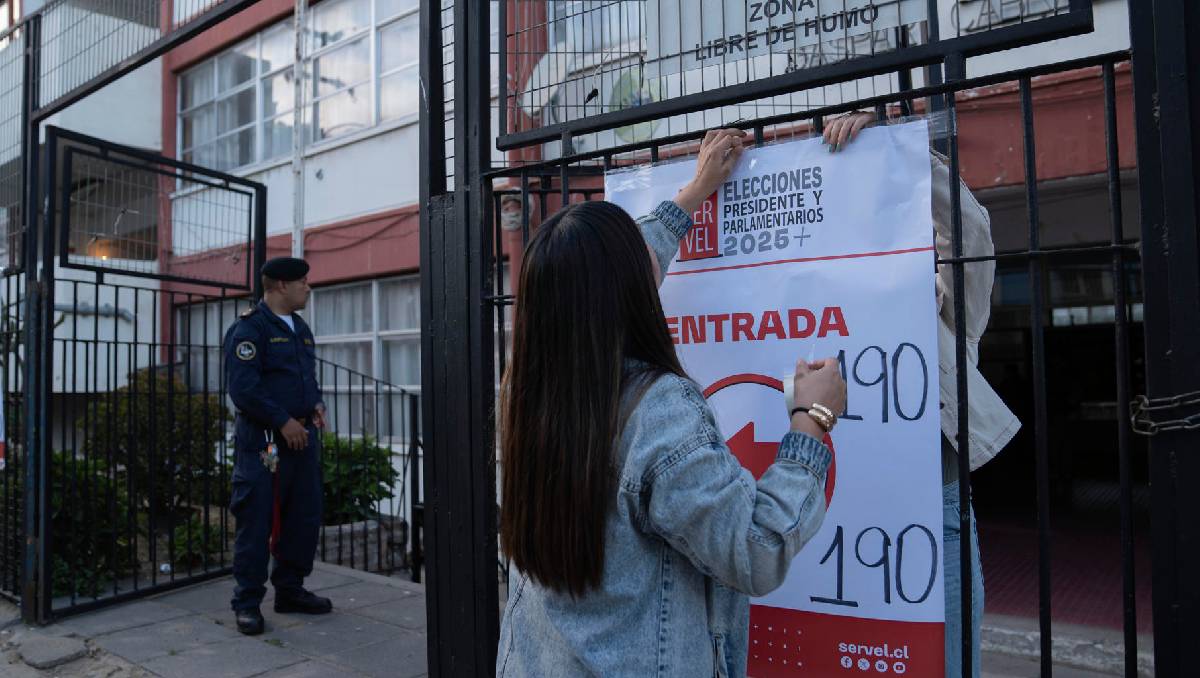 Una persona pega un cartel afuera de un centro de votación este domingo, en Valparaíso (Chile). EFE