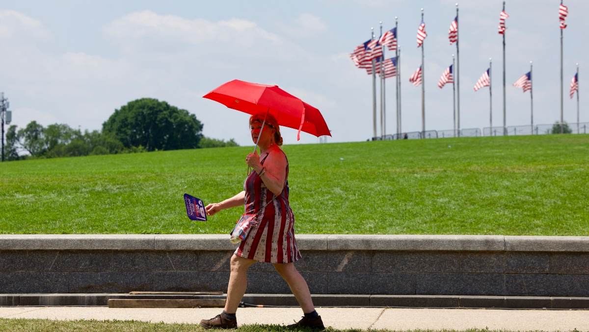 Una mujer utiliza un paraguas mientras la gente sobrelleva el calor extremo en el National Mall. | AFP